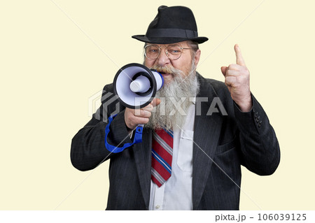 Portrait of aged senior businessman giving a speech in megaphone. Pastel yellow background. 106039125
