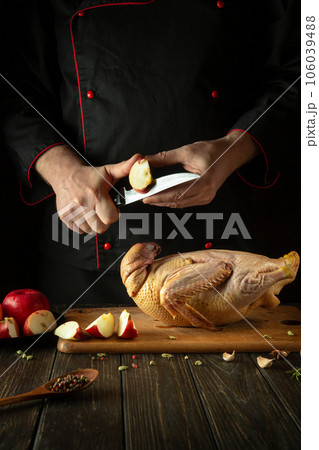 The chef cuts apples with a knife to add to raw duck before roasting in the oven. Cooking a national dish in the kitchen of a restaurant by the hands of a cook 106039488