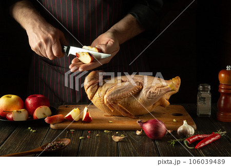 Cooking duck for lunch by the cook hands. Raw duck with apples and spices on the kitchen table. The chef cuts an apple Cooking duck for lunch by the cook hands. Raw duck with apples and spices on the kitchen table. The chef cuts an apple 106039489