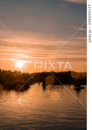 Stand up paddle boarding or standup paddleboarding on quiet lake at sunrise with beautiful colors during warm summer. Active women, close-up of water surface. 106040137