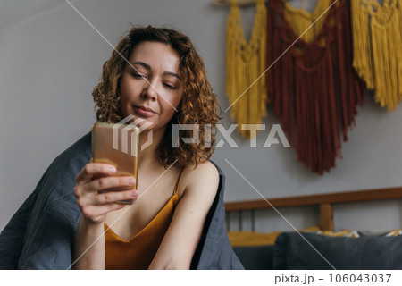 Young woman using phone, relaxing in bed, checking social media after waking up 106043037
