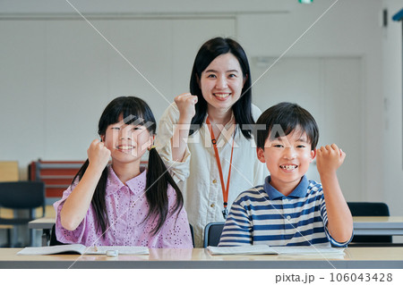 ガッツポーズする小学生の生徒と若い塾講師 106043428