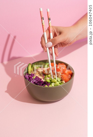 Hands eating poke bowl with salmon on pink background 106047405