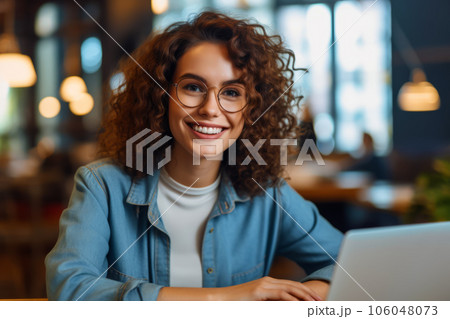 Woman with curly hair and glasses is smiling while using laptop computer. Generative AI 106048073
