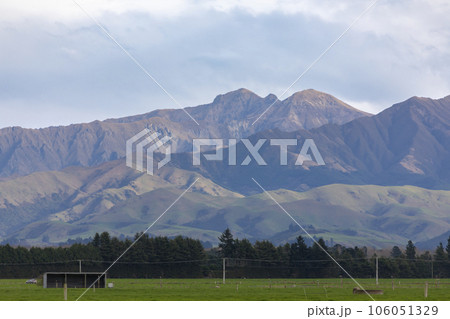 Photograph of a mountain range located behind a large green agricultural field in New Zealand Photograph of a mountain range located behind a large green agricultural field in New Zealand 106051329