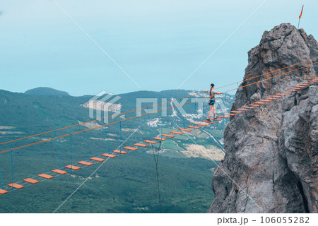 The girl walks on the suspension bridge between the tops of the mountains. The girl walks on the suspension bridge between the tops of the mountains. 106055282