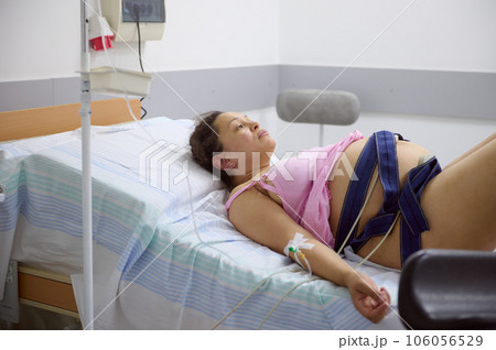 Birthing mother with a belt around her belly checking the heartbeat and pulse of future baby, during the labor process 106056529