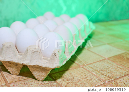 Chiken white eggs in a cardboard tray on a green back wall 106059519