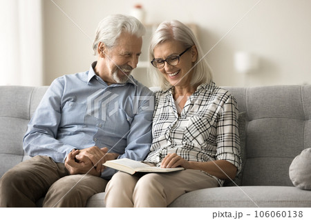 Happy retired elderly couple discussing open book on home sofa Happy retired elderly couple discussing open book on home sofa 106060138