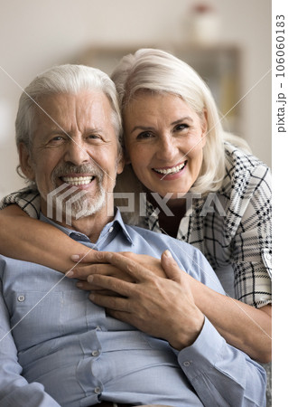 Happy cheerful mature couple hugging on sofa for home portrait Happy cheerful mature couple hugging on sofa for home portrait 106060183