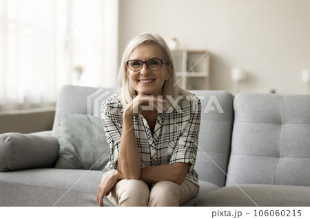 Happy blonde mature woman in stylish eyeglasses sitting on couch Happy blonde mature woman in stylish eyeglasses sitting on couch 106060215
