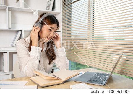 Beautiful young asian woman watching live video or video call of teacher teaching on laptop in her home, Take notes of important conversations and messages during the teacher's teaching. 106061402