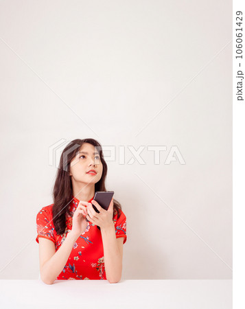 Smiling young asian woman in traditional cheongsam qipao dress using a smart phone isolated on white background. Smiling young asian woman in traditional cheongsam qipao dress using a smart phone isolated on white background. 106061429