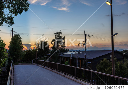 2023夏奈良市住宅街の夕景　街灯がつき始めた遊歩道の歩道橋と遠景の夕焼け空に浮かぶ入道雲 106061473