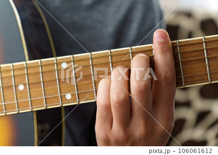 Guitarist male playing acoustic guitar sitting at desk, selective focus. Creative musician enjoying leisure activity in apartment. 106061612