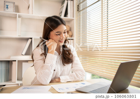 Woman using laptop to work or do homework at home with smiling face in her office, Creating happiness at work with a smile, Live performance or vdo call with laptop, Work from home. Woman using laptop to work or do homework at home with smiling face in her office, Creating happiness at work with a smile, Live performance or vdo call with laptop, Work from home. 106063801