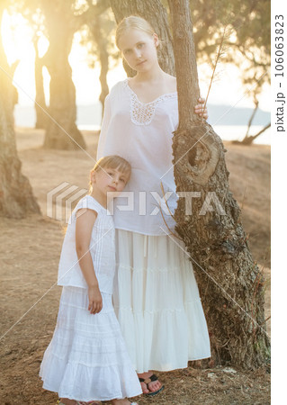 Portrait of two sisters, kid and teenage girl in white clothes against background of park 106063823