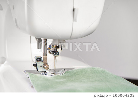 Modern sewing machine presser foot with green fabric and thread, closeup, macro 106064205