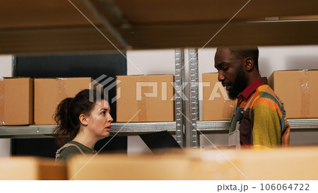 Team of supervisors checking stock list and doing inventory in storage room, diverse people verifying logistics for merchandise distribution. Man and woman reviewing products. Handheld shot. 106064722
