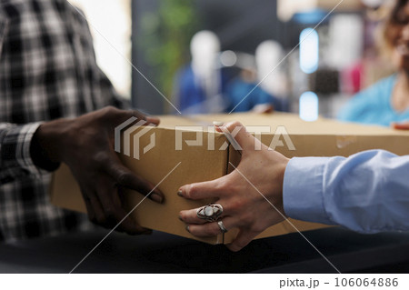 African american customer holding cardboard box at counter desk, after buying fashionable merchandise. Stylish man shopping for elegant clothes, discussing about material in modern boutique 106064886