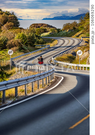 Couple rides a motorcycle on a winding Atlantic road in Norway. 106069290