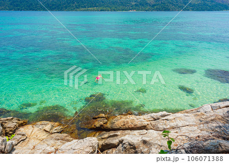 Rocks and turquoise water with a lone swimmer in it by Sunset Beach in Ko Lipe, Thailand. April 106071388