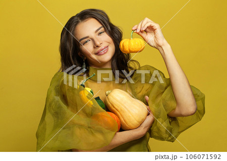 Attractive woman brunette holding pumpkin on colorful yellow background Attractive woman brunette holding pumpkin on colorful yellow background 106071592