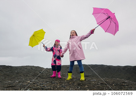 Happy funny children with pink and yellow umbrella outdoors. Girls wearing pink raincoat Happy funny children with pink and yellow umbrella outdoors. Girls wearing pink raincoat 106072569