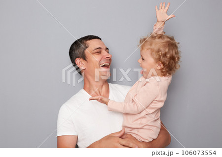 Laughing man standing with his infant daughter having fun smiling expressing happiness enjoying spending time together baby raised arrm showign how tall is she. Laughing man standing with his infant daughter having fun smiling expressing happiness enjoying spending time together baby raised arrm showign how tall is she. 106073554