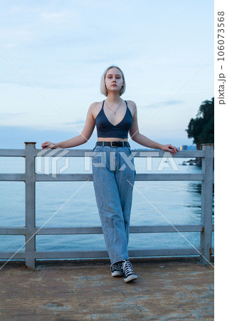Blonde woman standing on pier on the background of blue sea and cloudy sky 106073568