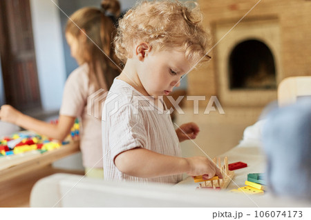 Smart educational toys. Building wooden constructions. Domestic care and learning. Curious wavy haired blonde toddler baby playing wooden educational toys at home interior. 106074173