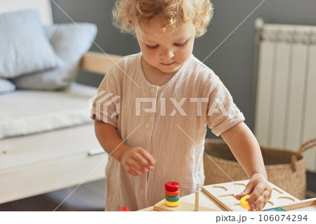 Cognitive development puzzles. Montessori learning approach. Wooden construction set. little blonde baby girl palying with wooden sorter toys at home interior 106074294