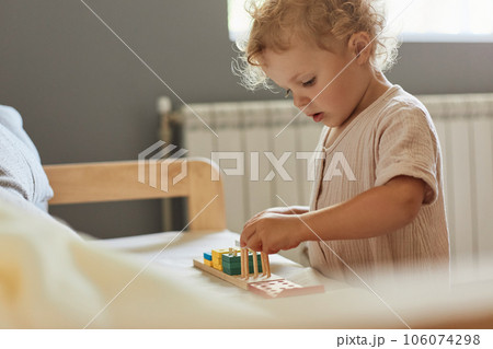 Montessori learning materials. Active playtime fun. Happy childhood memories. Toddler little blonde baby girl palying with wooden sorter toys at home interior. Montessori learning materials. Active playtime fun. Happy childhood memories. Toddler little blonde baby girl palying with wooden sorter toys at home interior. 106074298