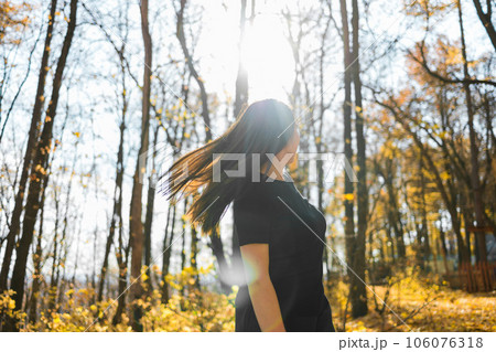 Cute young woman with long fluffy hair dancing in a park at sunset. Beautiful young woman with brown hair dance in a forest at sunset. Freedom and season nature concept. Soft focus Cute young woman with long fluffy hair dancing in a park at sunset. Beautiful young woman with brown hair dance in a forest at sunset. Freedom and season nature concept. Soft focus 106076318