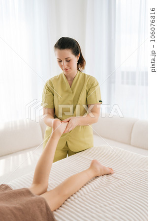 Vertical portrait of professional orthopedic female doctor doing orthopedic leg exercises of teenager girl client, examining and massaging patient foot. Professional masseur massaging legs. 106076816