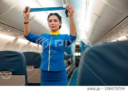 Female flight attendant with seatbelt standing in aircraft cabin Female flight attendant with seatbelt standing in aircraft cabin 106078704