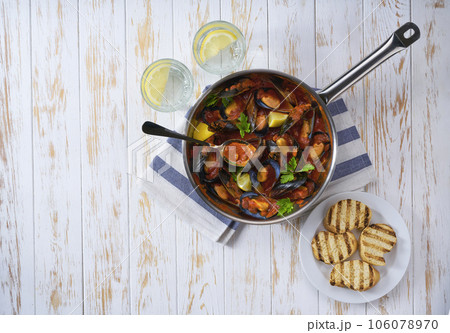 Steamed mussels in shells and tomato sauce with roasted bread and greens on a white table, top view. Steamed mussels in shells and tomato sauce with roasted bread and greens on a white table, top view. 106078970
