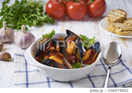 Traditional tomato soup with mussels with and toasted baguette on a white table. 106078982