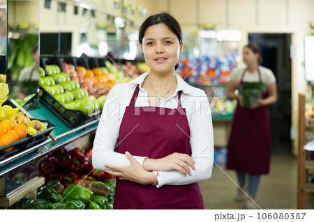 Friendly woman vegetable shop seller posing behind counter Friendly woman vegetable shop seller posing behind counter 106080387