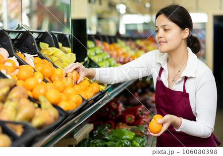 Asian female seller in apron chooses ripe mandarin 106080398