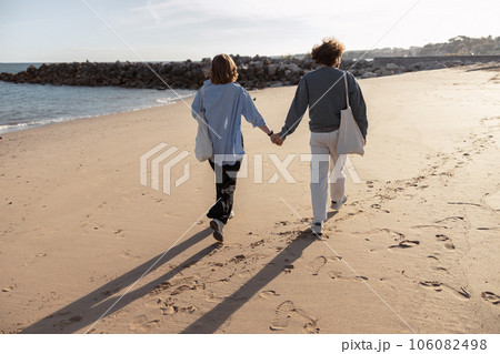 Rear view of couple in love is walk holding hands across the sunny beach 106082498
