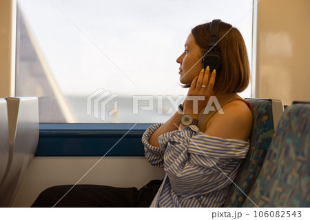 Woman in headphones while traveling in public transport and looking view outside the window Woman in headphones while traveling in public transport and looking view outside the window 106082543