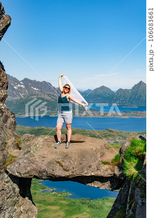 Brave traveler woman standing on hanging stone between rocks. Djevelporten in Norway Lofoten islands 106083661