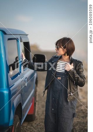 オーバーオールにライダースサングラス姿の女性が車の方を見て立っている 106089399