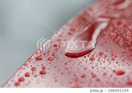 Rain droplets on red sports car surface with hydrophobic treatment 106091104