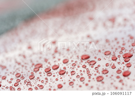 Rain droplets on red sports car surface with hydrophobic treatment 106091117