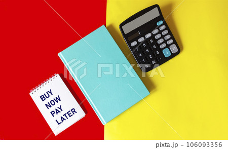 Notepad with the words BUY NOW PAY LATER on a red and yellow background with a green diary  106093356