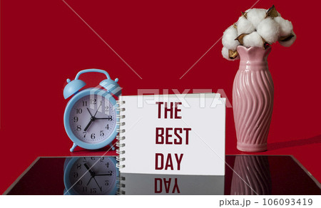 the BEST DAY, the text is written on a notebook, next to a bouquet of flowers and an alarm clock. the BEST DAY, the text is written on a notebook, next to a bouquet of flowers and an alarm clock. 106093419