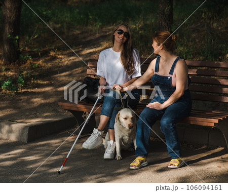Blind caucasian woman sitting on bench with guide dog and pregnant friend.  106094161