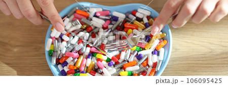 Female hands holding table knife and fork above heart shaped bowl with pile of medicine. 106095425